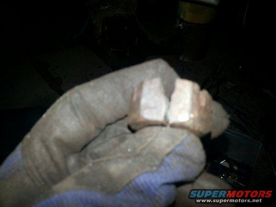 Gloved hand holding two rusty metal nuts, one cracked