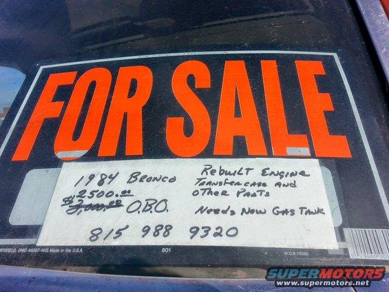 For sale sign on a vehicle windshield, listing '1984 Bronco', price, and contact info