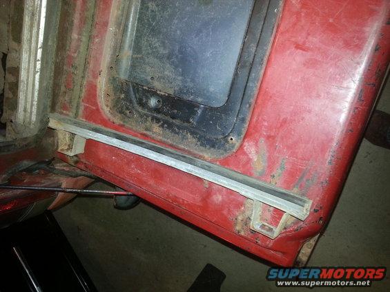 Red vehicle door frame with rust and a dark window opening. A metal trim piece is visible