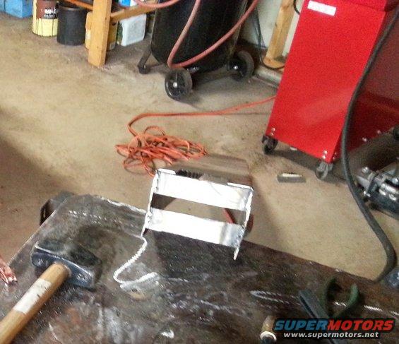 Metal bracket with two horizontal bars on a workbench, next to a sledgehammer and wire
