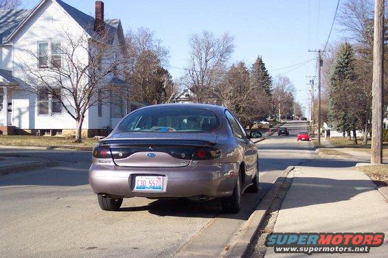 1996 Ford Taurus sedan, rear view, parked on street, light purple color, clear sky