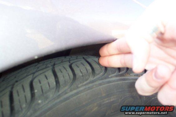 Close-up of tire tread and fender gap with a hand checking clearance