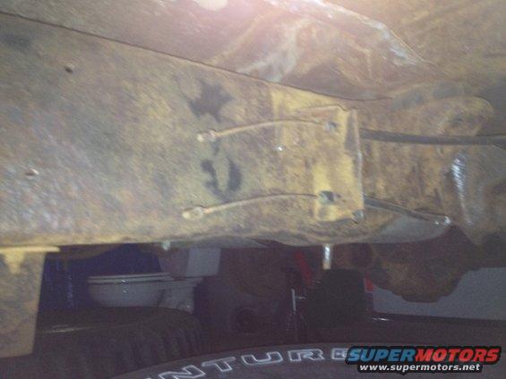 Underbody view of rusty frame rails and suspension parts, with a tire visible at the bottom