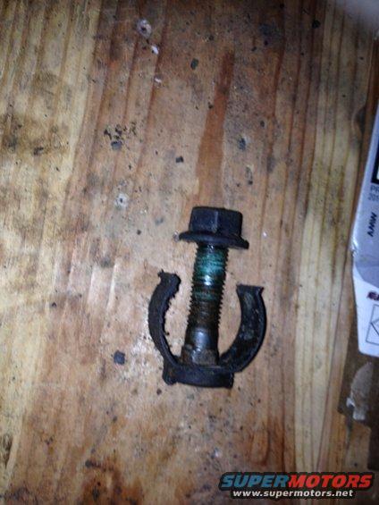 Bolt with green thread locker and broken clamp on wooden surface