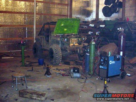 Off-road vehicle with green hood open, in a garage with welding equipment