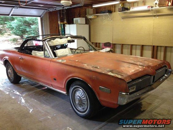 Orange 1968 Mercury Cougar convertible in a garage, showing rust and primer on the hood
