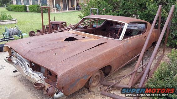 Rusty coupe with holes in hood and roof, front end damaged