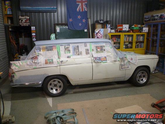 Station wagon covered in newspaper and tape, likely for painting. Garage setting with tools and shelves