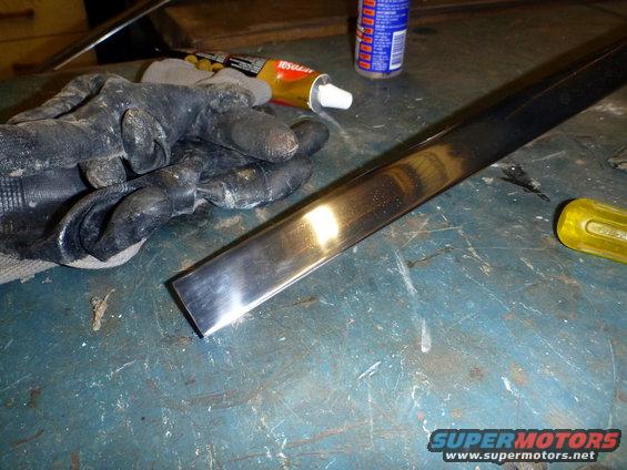 Chrome trim piece on a workbench with black gloves, glue tube, and yellow screwdriver