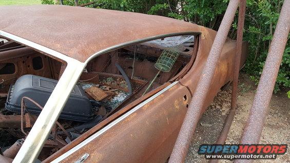 rusted out car interior with broken windows and debris inside