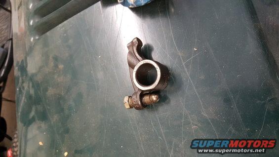 Engine valve rocker arm with bolt and nut on a green surface