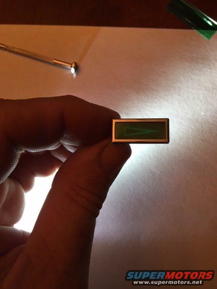 Rectangular green gauge indicator with a white triangle, held by fingers