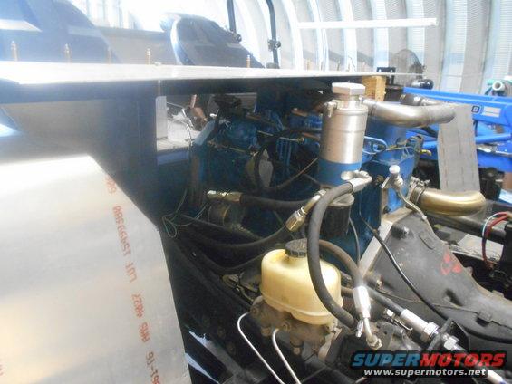 Engine bay with blue engine block, hoses, and brake fluid reservoir. Some metal sheeting is in the foreground