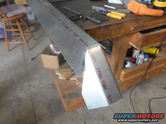 Bent metal piece with red text markings on a workbench, tools and supplies visible