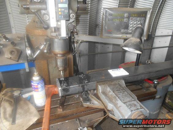 Milling machine drilling into metal stock held in a vise, with a spray can and hammer nearby