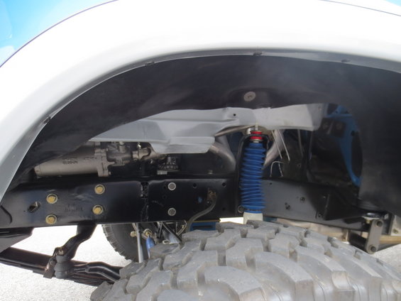 Close-up of a truck's front wheel well showing suspension components, including a blue shock absorber and leaf springs