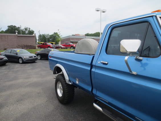 Side view of a blue pickup truck with a grey bed cover, parked in a lot with other vehicles and a McDonald's in the background