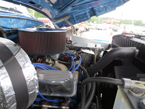 Close-up of a blue Ford truck's engine bay with a large air filter and chrome valve covers. The hood is open