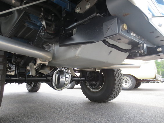 Undercarriage view of a truck showing the rear axle, exhaust, and a hitch receiver; a yellow vehicle is visible in the background