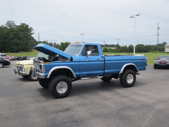 Blue Ford pickup truck with hood open, parked next to a yellow truck