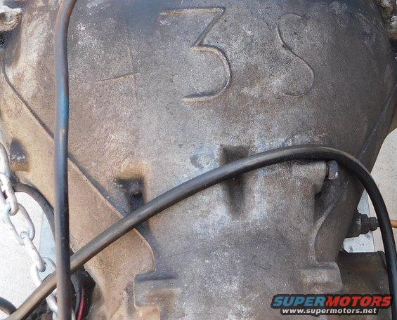 Close-up of a transmission casing with '3S' cast into it. A chain and hoses are visible