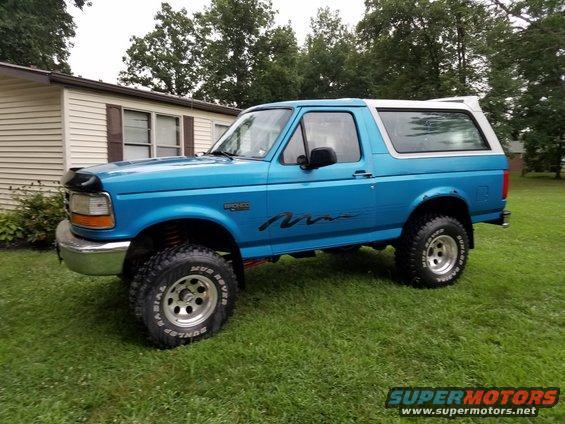 Blue Ford Bronco with lifted suspension, aftermarket wheels, and "Mud Rover" tires parked on grass
