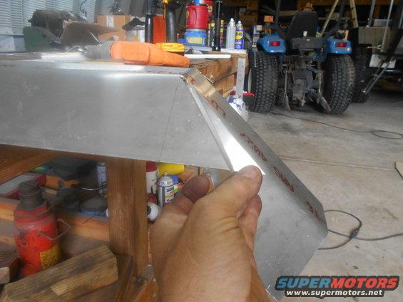 Hand shaping aluminum panel with red markings, tractor in background