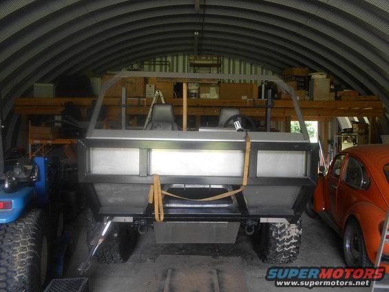 Custom amphibious vehicle with seats and steering wheel, parked next to an orange Volkswagen Beetle in a garage