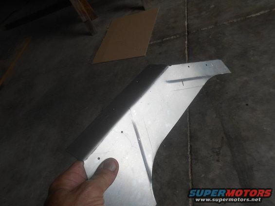 Metal car fender part held by hand, with visible cut lines and drill holes
