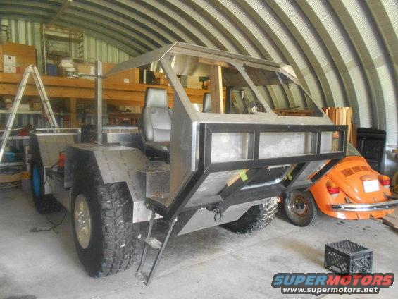 Custom metal vehicle build in a garage, with an orange VW Beetle behind it