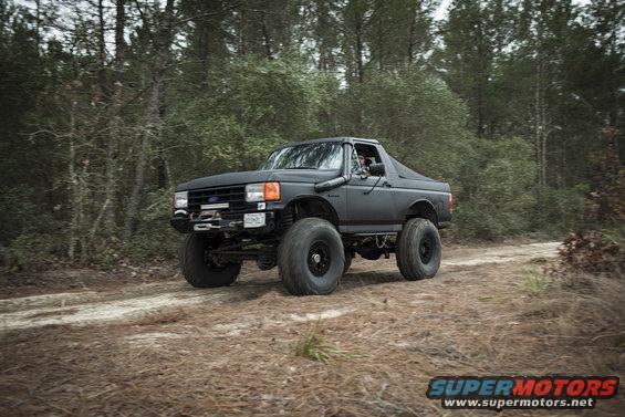 Black lifted 1989 Ford Bronco with snorkel driving on dirt road