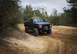 1989 Ford Bronco - Modified 1987 Ford F-150 truck navigating a dirt path in a wooded area.