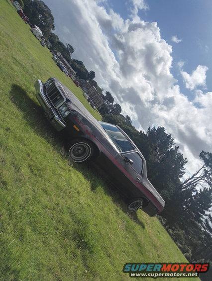 Dark red 1974 Ford Ranchero with a red stripe, parked on a grassy hill