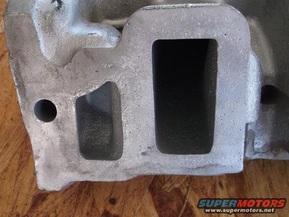 Aluminum engine part with two rectangular openings and a circular hole, on a wooden surface