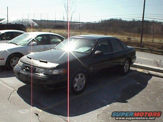 Dark 1999 Ford Taurus sedan parked, 3q-front view, with hood cover
