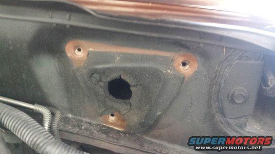 Close-up of a rusted hole in a car's firewall, with mounting holes around it
