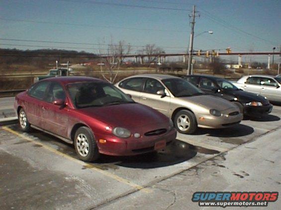 Red 1999 Ford Taurus parked next to a gold 1999 Ford Taurus and a black car
