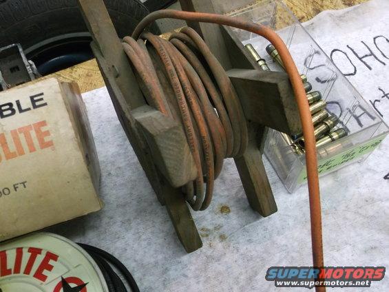 Wooden hose reel with coiled orange hose, box labeled 'ABLE LITE', and a clear container of bullets