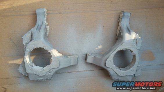 Pair of gray suspension knuckles with masking tape, on a wooden surface