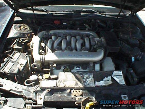 Engine bay with V6 engine, intake manifold, battery, and various hoses and components visible