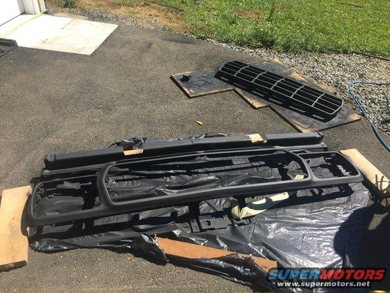 Two black car grilles and trim pieces laid out on asphalt