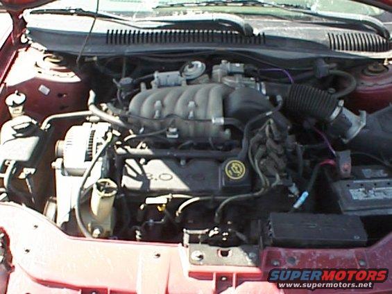 Red 1999 Ford Taurus engine bay with 3.0L V6 engine visible. Battery and alternator also in view