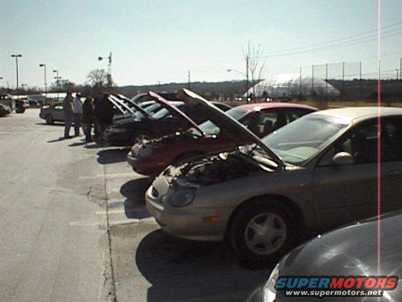 Silver 1999 Ford Taurus 3q-front view with hood open. Several other cars are parked nearby