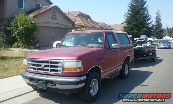 Red 1995 Ford Bronco parked on street, towing a boat on a trailer