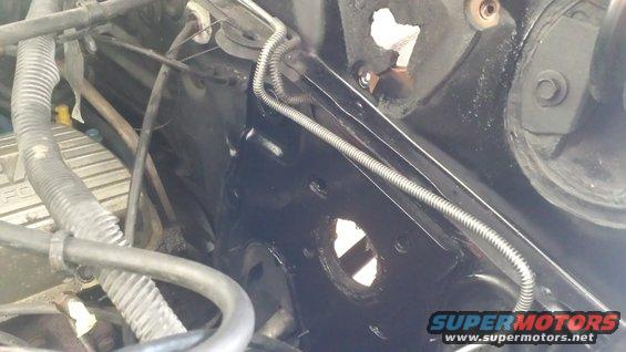 Close-up of engine bay with black painted metal, hoses, and wiring