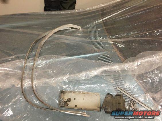 Car hood with vents covered in plastic, along with trim pieces and a license plate bracket