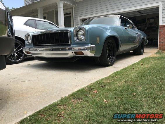 Light blue coupe with black grille and wheels parked in driveway next to a white car