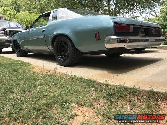 Blue 1975 Chevrolet Chevelle coupe, rear 3/4 view, black wheels, chrome bumper, parked on concrete driveway