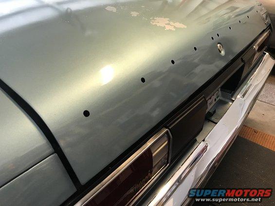 Light blue car trunk with peeling paint, showing holes for a badge and taillight trim