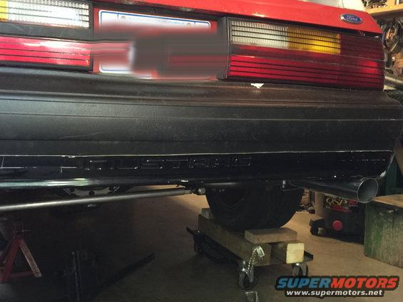 Rear of a red 1983 Ford Mustang with 'MUSTANG' text on the bumper and a new exhaust pipe